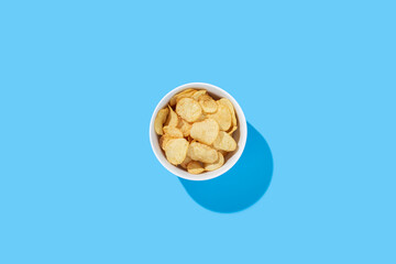 Potato chips in a bowl on a blue background. Top view, flat lay.