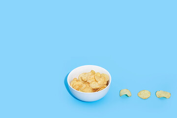 Potato chips in a white bowl on a blue background. Top view, flat lay.
