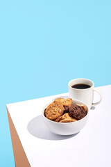 Cup with coffee, cookies in a bowl on a white-blue background. Top view, flat lay.