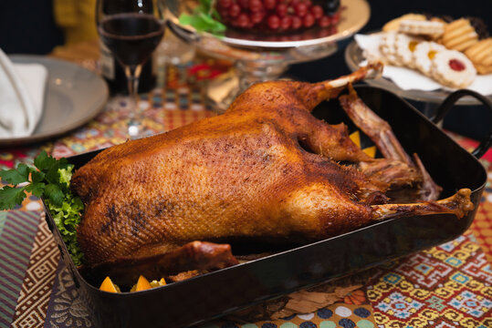 Ein knuspriger G&auml;nsebraten auf einem festlich gedeckten Tisch, umgeben von rustikalen Beilagen wie Rotkohl, Kartoffeln und Kr&auml;utern, in einer gem&uuml;tlichen, traditionellen Atmosph&auml;re."