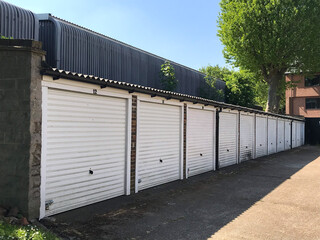 London, England - May 8 2020 - A row of closed white parking garage doors in suburban London, under a sunny blue sky.  Image has copy space.