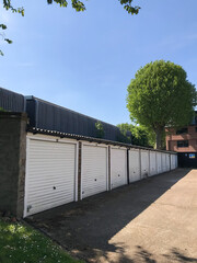 London, England - May 8 2020 - A row of closed white parking garage doors in suburban London, under a sunny blue sky.  Image has copy space.