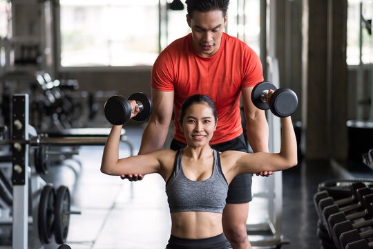 personal trainer coaching dumbbell to Asian girl in gym