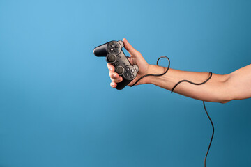 Play computer games ,become a professional gamer. A man's hand holds a gamepad with a wire, a photo on a blue background - Powered by Adobe
