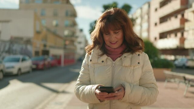 Middle age redhead woman smiling confident using smartphone at street