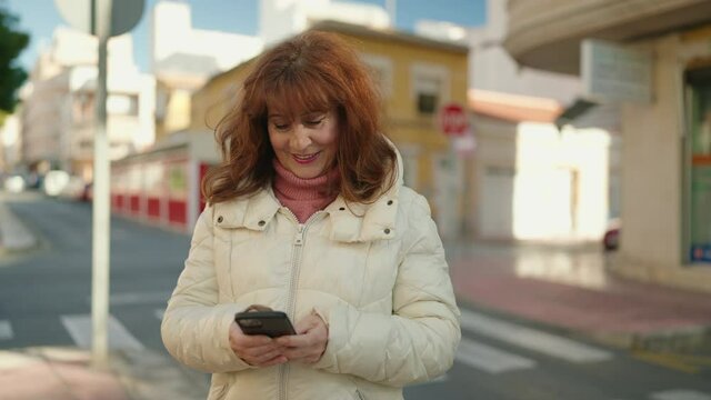 Middle age redhead woman smiling confident using smartphone at street
