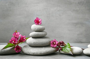 Spa stones with green leaf and weigela flowers on grey background.