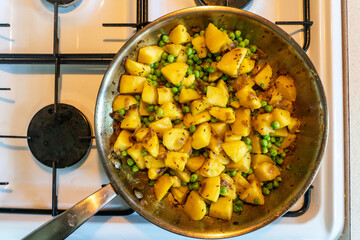 Tasty and spicy potatoes and peas vegetarian North Indian dish in a stainless-steel frying pan on a gas cooker. Alu matar sabzi - obrazy, fototapety, plakaty