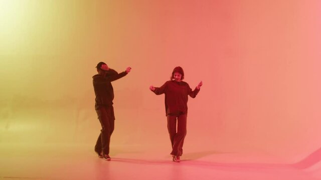 Professional choreographers dancing hip hop on color changing neon background. Man and woman dancers showing movements, pair dance, duet. Modern dance school for teenagers.