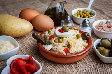 Spanish style Russian salad, also known as Olivier salad, accompanied by the main ingredients for its preparation.