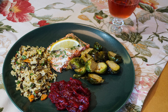 Appetizing, beautifully presented gourmet meal of baked salmon, rice pilaf, vegetable, fresh cranberries, with glass of rose wine.