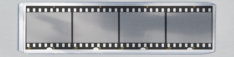long 35mm film strip behind transparent plastic top loader case on white paper background.