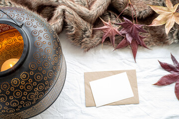Autumn, winter composition.Blank greeting card mock-up on white linen.Lantern, maple leaves, plaid.Winter wedding, thanksgiving concept.Top view, flat lay
