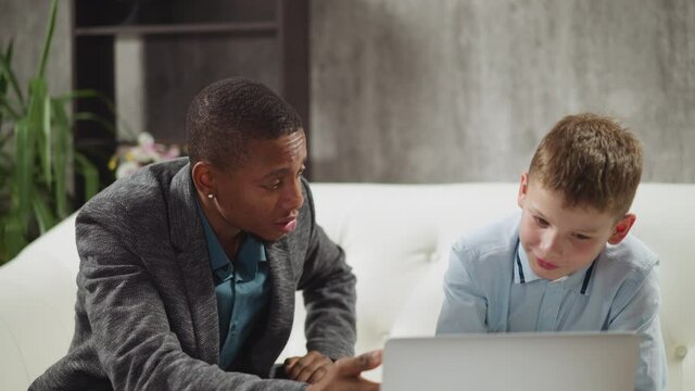 Native speaker English teacher and happy primary school pupil watch and discuss educative video via laptop computer at home lesson slow motion