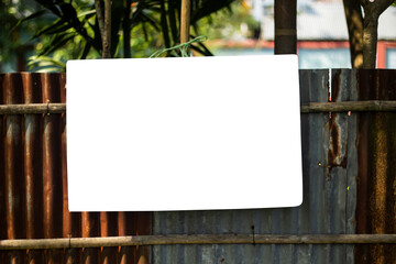 A white signboard hangs along with the old tin, bamboo fence and the background behind it is blur green.