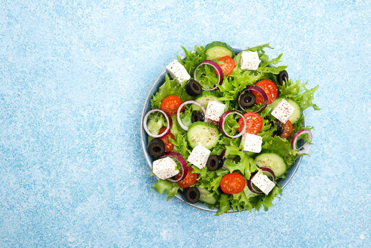 Greek salad with tomatoes, cucumbers, olives and feta cheese in a plate on a concrete background, top view