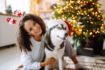 Happy woman celebrating winter holidays with a dog Husky on the background of the Christmas tree. New year. Christmas surprise.