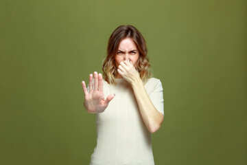 Bad smell. Young girl pinch nose showing stop gesture, feel disgust on green background. Toxic odor, terrible perfume