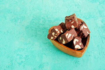 Sliced homemade fudge chocolates made from dark chocolate, condensed milk and hazelnuts on a turquoise concrete background. Candy recipes. American cuisine.