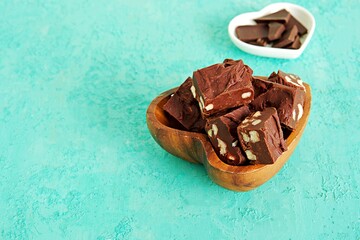 Sliced homemade fudge chocolates made from dark chocolate, condensed milk and hazelnuts on a turquoise concrete background. Candy recipes. American cuisine.