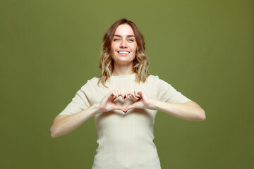 Beautiful young caucasian girl with showing heart gesture, happy female folded hands in love sign....