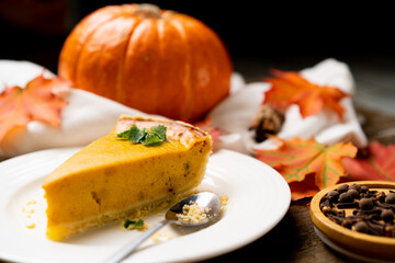 a piece of American pumpkin pie on a white plate and a wooden table