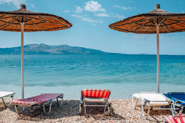 View of empty beach - sun beds and umbrella near sea water, mountains on the horizon and blue sky. Summer landscape of abandoned resort.