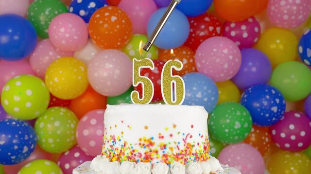 Cake with burning candles number 56. Celebration cake on a bright festive background of colorful balloons.