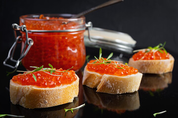 Delicious fresh red caviar with baguette toasts on dark background