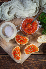 Delicious fresh red caviar with baguette toasts on wooden background. Top view