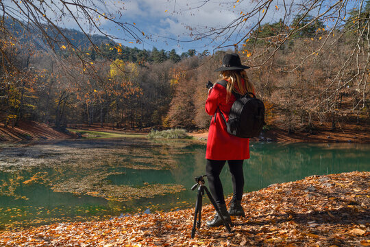 Back view of female photographer in red jacket and black hat taking photos in sevenlakes (yedigoller), Bolu, Turkey