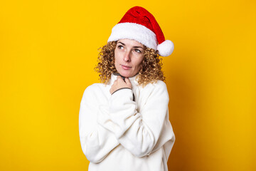 Curly young woman in santa claus hat on a yellow background.