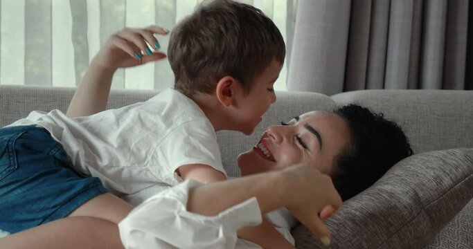 A happy family of mom and a son, resting together on the couch, these preschoolers sleep on their mother's tummy, hugging at home, the mother stroking the child on the head.