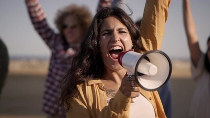 At protest, woman shouts with megaphone raising her fist in crowd. People demonstrating for their rights.