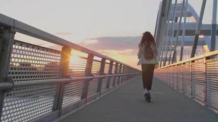 A young woman riding her electric scooter on the bridge - Powered by Adobe
