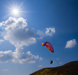 paraglider flying above mount slope on suny cloudy sky background, extremal sport background