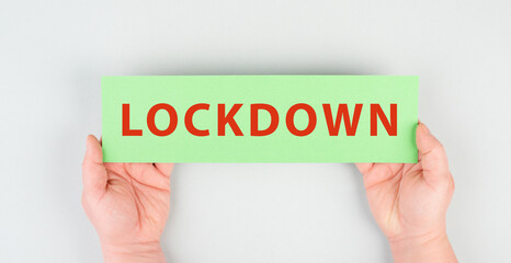 The word lockdown is standing on a green paper, Covid-19 pandemic regulations, hands holding the message