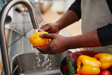 Close up of African-American man washing fresh vegetables while cooking in kitchen, copy space - Powered by Adobe