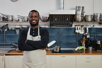 Waist up portrait of African-American man smiling at camera while working in professional kitchen, copy space