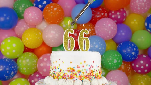 Cake with burning candles number 66. A tasty celebration cake on a bright festive background of colorful balloons.