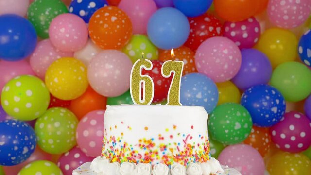 Cake with burning candles number 67. A tasty celebration cake on a bright festive background of colorful balloons.