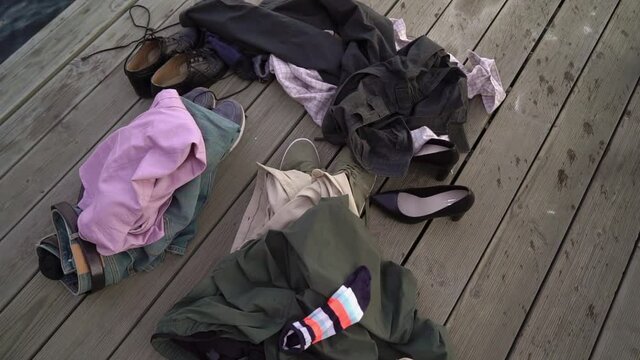 Clothes and shoes are on the pier. People undressed and swim naked in the lake in the evening at sunset or at night, skinny dipping. There are no people, only a shirt and pants. Naturist bathing.