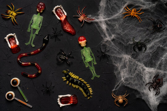 spider web, snakes, insects made of candy and marmalade on a black background, Halloween, top view