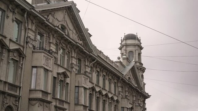 Old historic gray stone building in a European city. Cloudy day, rainy sky. Italian architecture in St. Petersburg. Windows, sculptures, roof and tower.