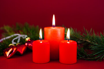 Scena natalizia con tre candele rosse accese e con addobbi natalizi a forma di cuore circondati da...