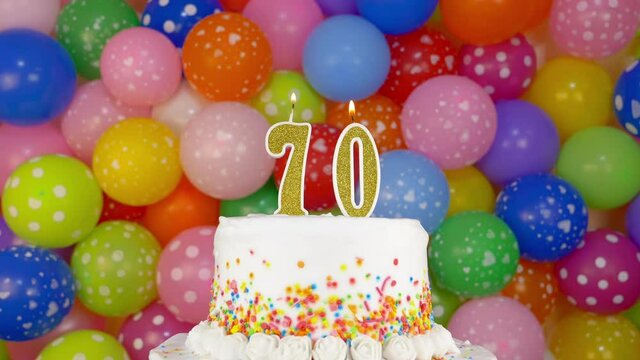 Cake with burning candles number 70. A tasty celebration cake on a bright festive background of colorful balloons.