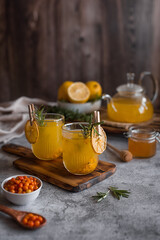 Sea buckthorn tea in a glass teapot and mugs with lemon, honey and ginger. Vertical photo.