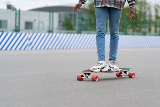 Woman riding longboard: cropped image of african female wear trendy sneakers shoes and blue jeans on skateboard. Ethnic young girl legs longboarding outdoors on city street. Urban lifestyle concept