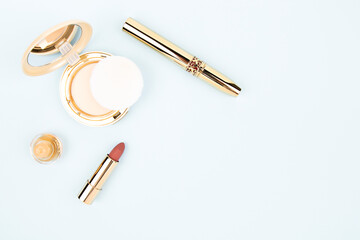 on a blue background cosmetics in a gold case lipstick, mascara and powder