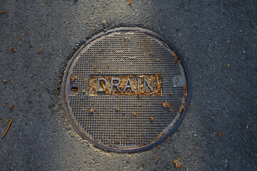 Round metal drain cover in an asphalt street, as a utility background
 - obrazy, fototapety, plakaty
